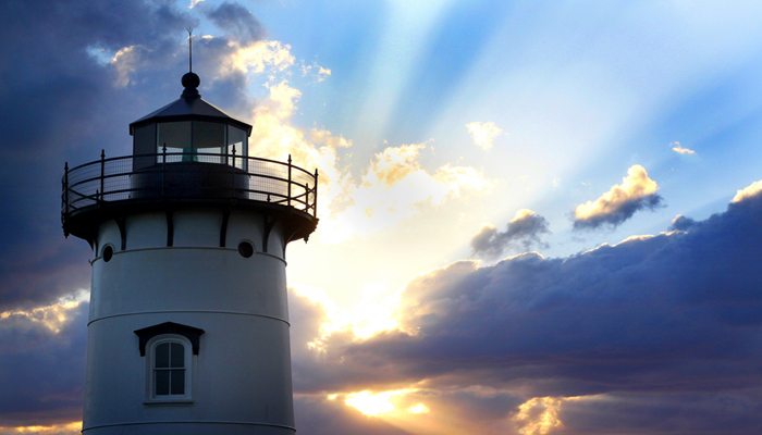 New England lighthouse with clouds and rays of sun