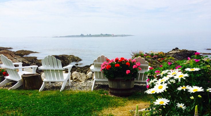 Four white adirondack chairs and flowers on viewpoint over an island off of Maine coast