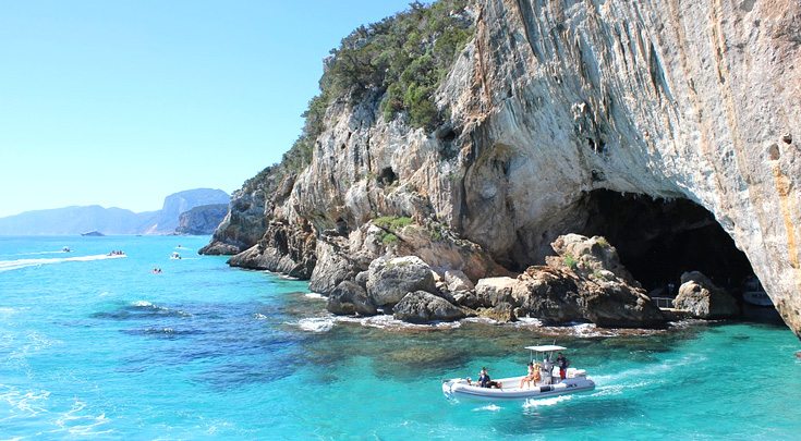 People on tender floating out of cave on turquoise blue water around Sardinia, Italy