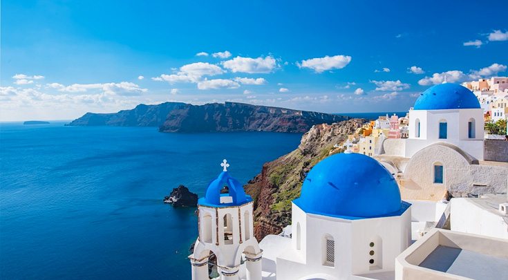 Iconic Greek blue-domed, white buildings overlook the water in The Cyclades, an island group in the Aegean Sea, southeast of mainland Greece