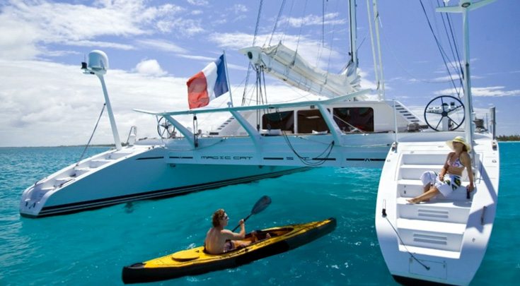 Kayaking up to woman lounging on steps of 82ft sailing yacht Catamaran Magic Cat