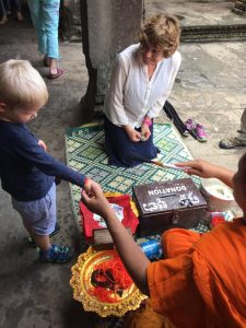 Child gives donation to Buddhist monk at Angkor Wat, Cambodia - w Karen Hughes