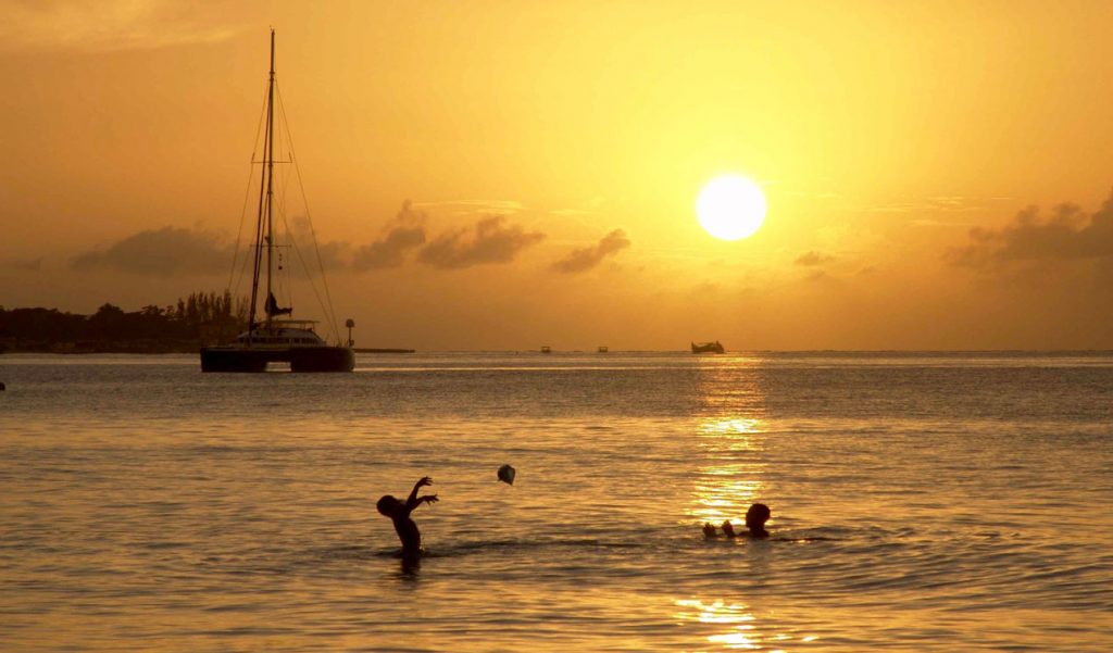 Father and son playing ball in water near Catamaran at golden Caribbean sunset