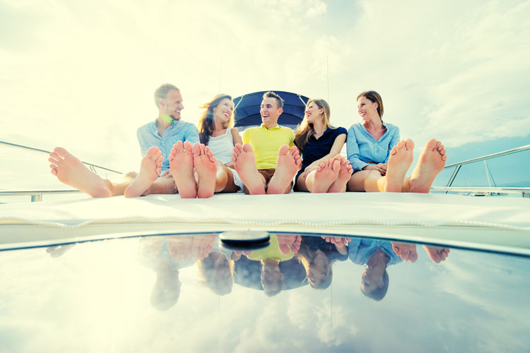 Millennial friendship and vacation. Group of laughing young people sitting on the yacht deck sailing the sea.