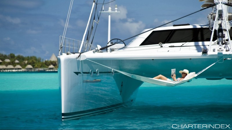 Woman reading magazine in hammock hanging off back of 82ft sailing yacht Catamaran Magic Cat