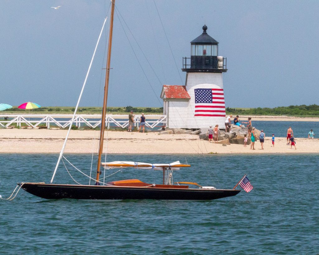 Sailboat moored off lighthouse beach with American flag Nantucket