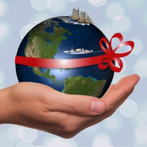 Globe in hand with sail boat, motor yacht and wrapped in a red ribbon