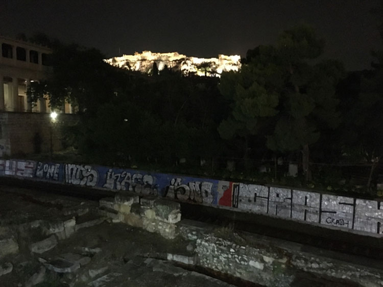 The Acropolis lit up at night with passenger train in the foreground