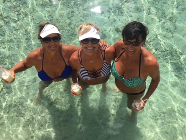 3 women holding drinks standing in Caribbean waters