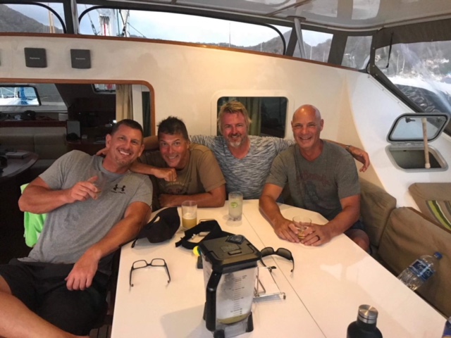 Four men at table inside sailing catamaran Adastra
