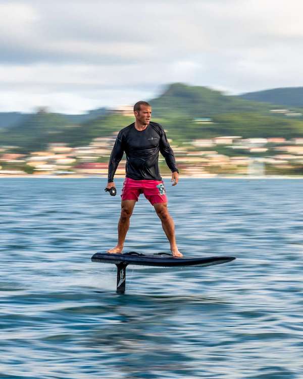 Colin Guinn riding an electric hydro foil board above the water of sailing catamaran TWIN FLAME