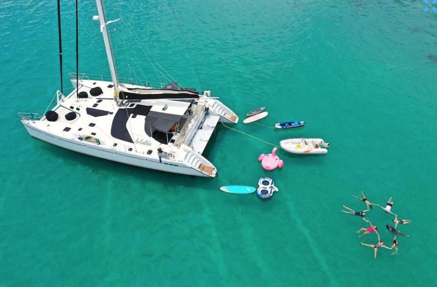 65ft Sailing catamaran Lolalita in blue-green water with toys and circle of floating friends and family