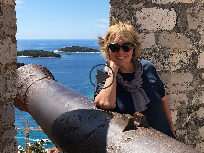 Carol Kent leaning on a cannon at a fortress in Croatia overlooking the sea