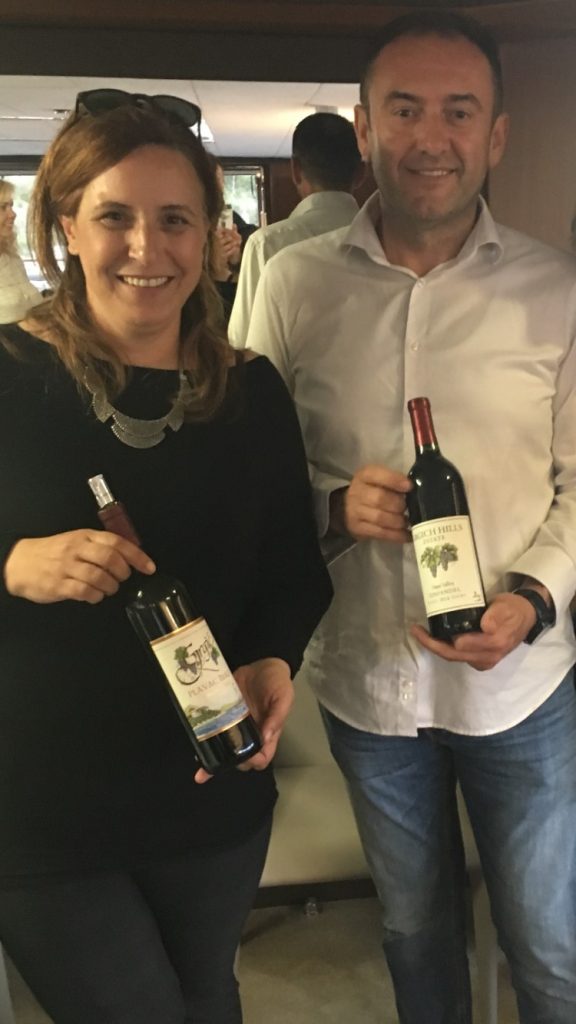 Two Mediterranean wine tasting guides holding bottles on board a boat