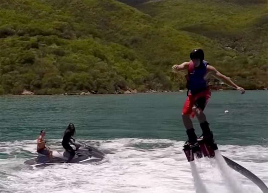 Man flyboarding above water while people on jet skis look on.
