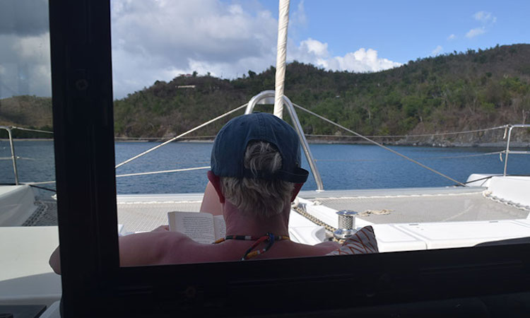 Doctor dad with cap on relaxes and reads on the aft deck of 52ft sailing catamaran STOP WORK ORDER in St. Croix, USVI