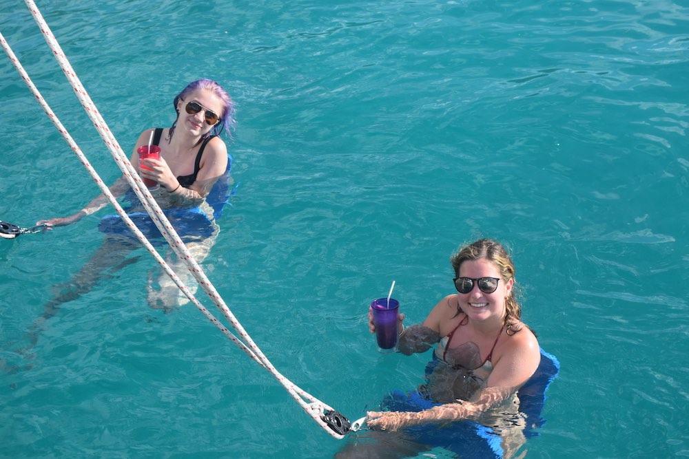 Mother and daughter Cuttino float in submerged chairs with drinks off sailing yacht charter catamaran SOUTHERN COMFORT (formerly STOP WORK ORDER) in St. Croix