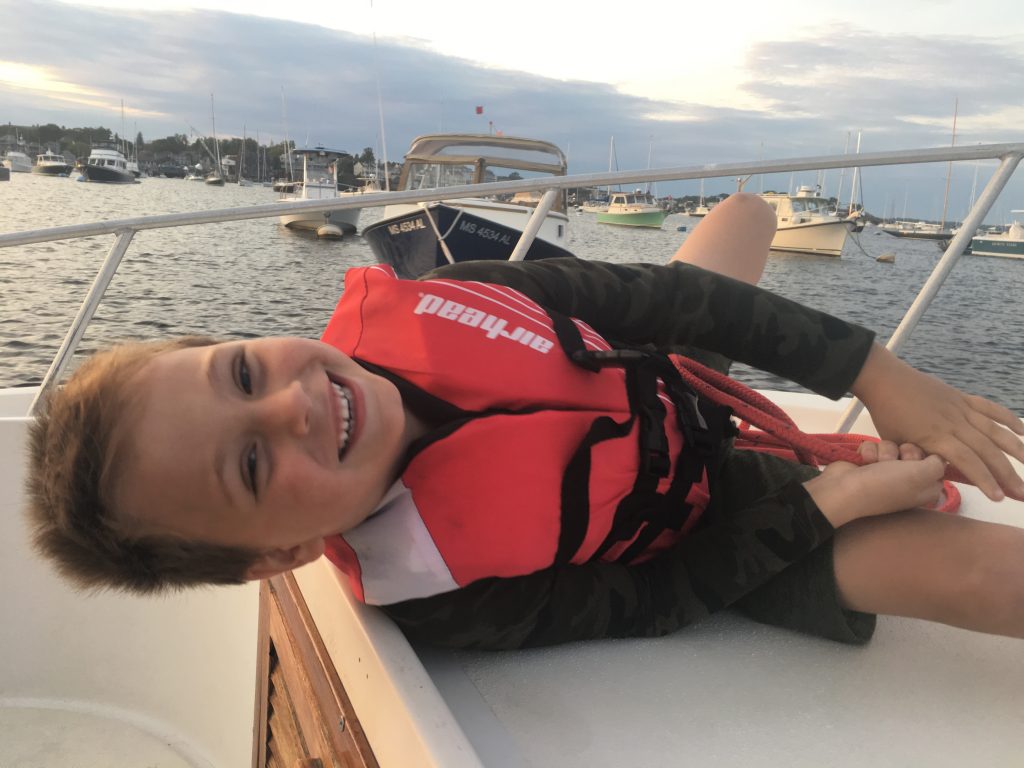 A young boy on a boat leaning sideways in Marblehead Harbor, Massachusetts