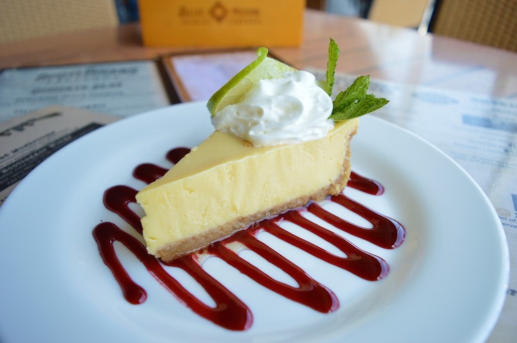 Slice of Key lime pie on a plate with red berry sauce, whipped cream and menus