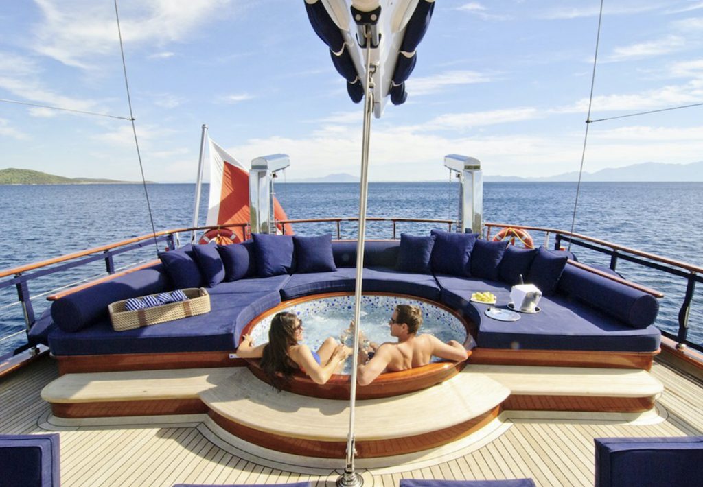 Couple in Jacuzzi on motor sailer yacht deck with blue seating
