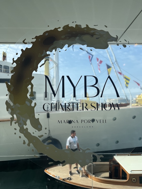 MYBA Charter Show logo at Marina Port Vell yacht in background through window in Barcelona 2023 photo©carolkent.com